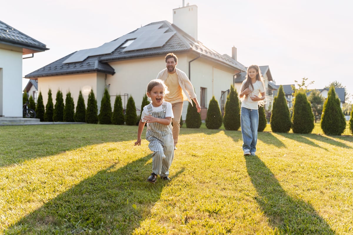 Father and his children playing and running on the lawn in front of their home with solar panels on the roof